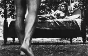 An outdoor scene of nude woman on bed as man approaches