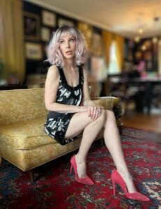 Adult performer Alex Foxe wearing a sexy dress and red heels.